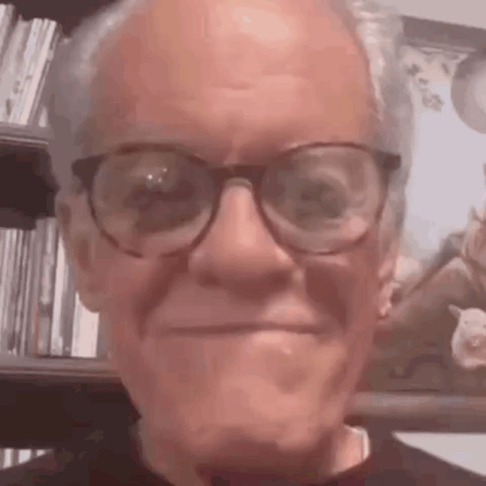 an elderly man wearing glasses is making a funny face in front of a picture .