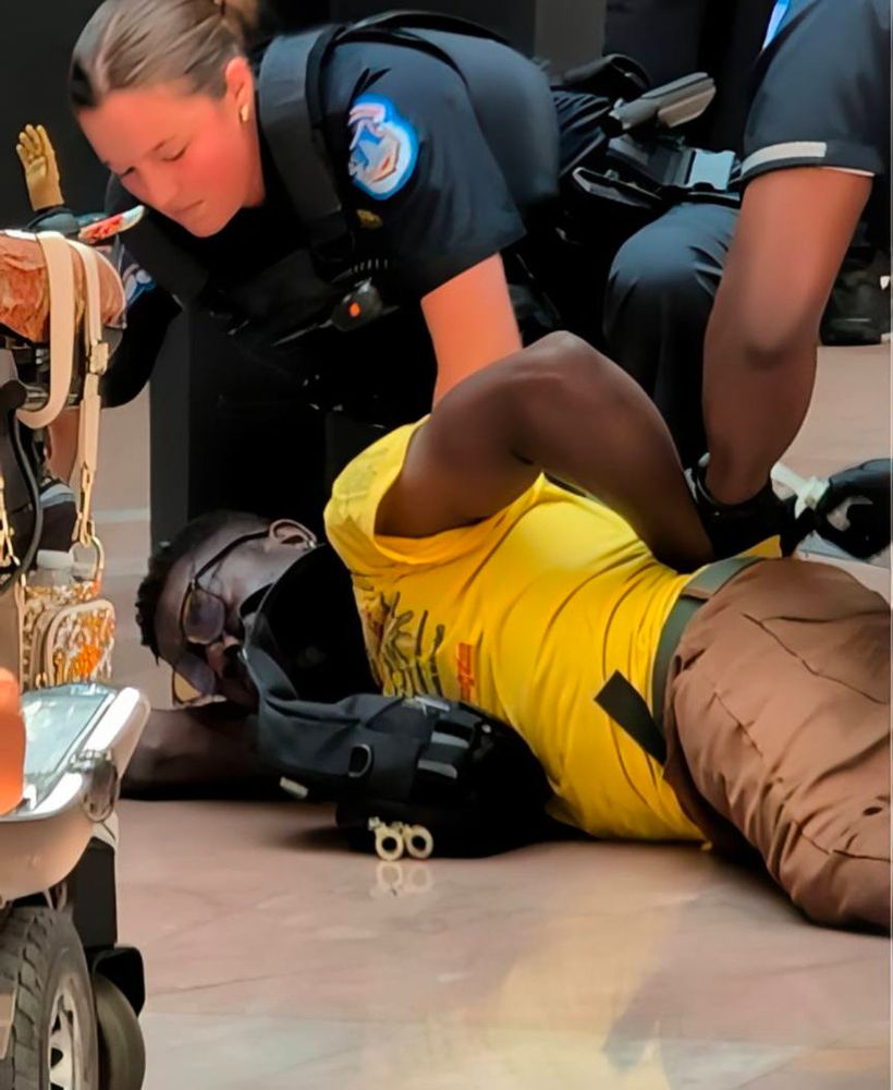 Two photographs of a disabled man with Brown skin and short gray and brown hair on the floor out of his wheelchair. He is being arrested by three armed Capitol Police. In the second picture they have him turned over with cuffs behind his back. The man is wearing a yellow ADAPT t-shirt and khaki pants.