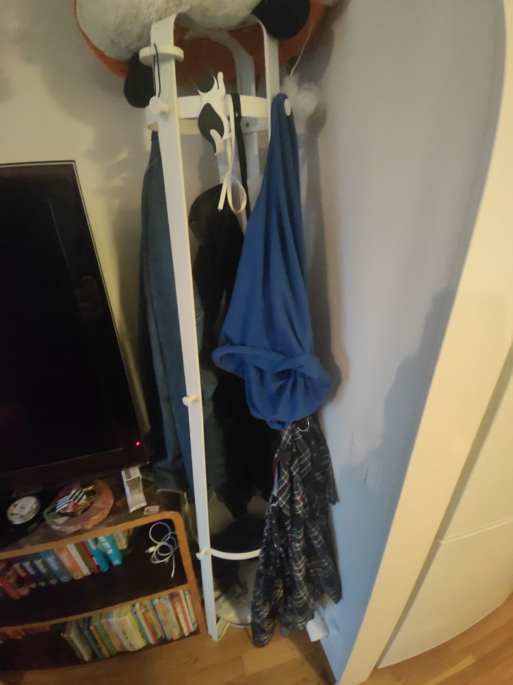 En tamburmajor i ett hörn bredvid en bokhylla. På den hänger ett par jeans, en kjol, ett diverse överdelar, samt en magnetisk krok i form av en katt där jag hänger glasögonen på svansen över natten 