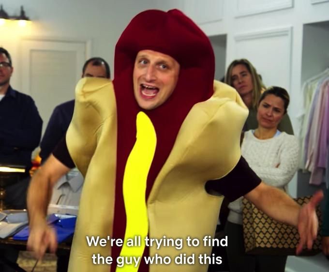 Man in hotdog costume saying “we’re all trying to find the guy who did this,” referring to driving a hotdog-shaped vehicle through the wall of the building