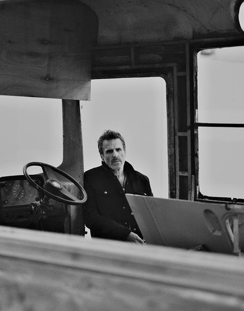 from that known photoshoot of Con O'Neill in black and white, he's wearing a black or dark coat, he has short hair. He's like out of the door of a big truck or something.