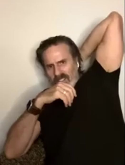 Con O'Neill in one of the lives. Wearing a black tshirt, longer hair and he has his elbow bent with his hand on the back of his head. the other hand on his front 
