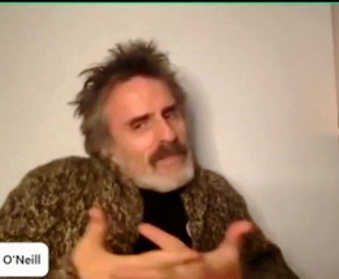 Con O'Neill shrugging with his hands together on the camera