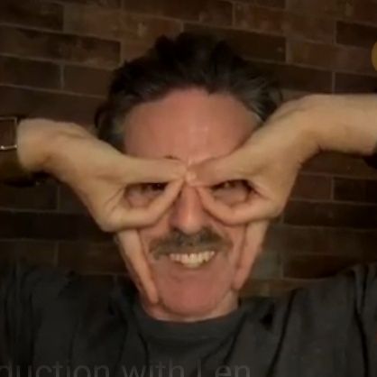 Con o'neill making glasses with his fingers turned upside down and smiling 