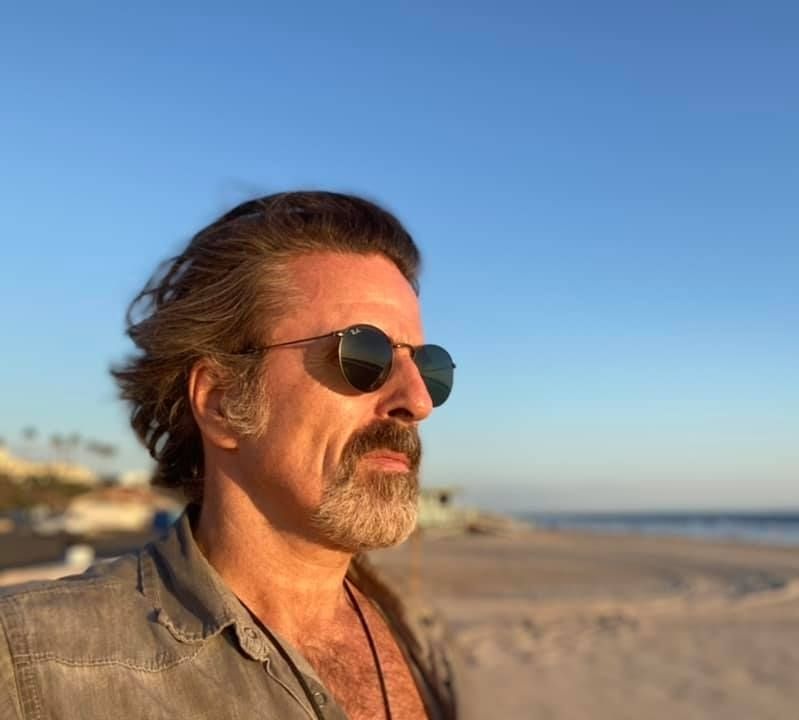 Con O'Neill on the beach, grey shirt open in the chest. dark sunglasses 