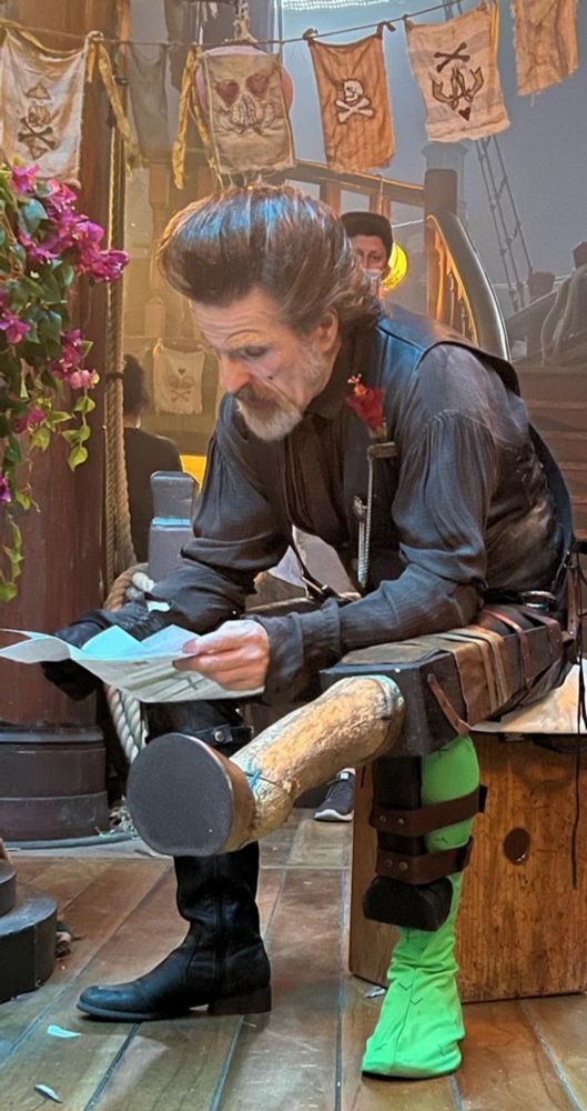 Con O'Neill bts picture as Izzy Hands, sitting with the green and unicorn leg, in Calypso's birthday.
