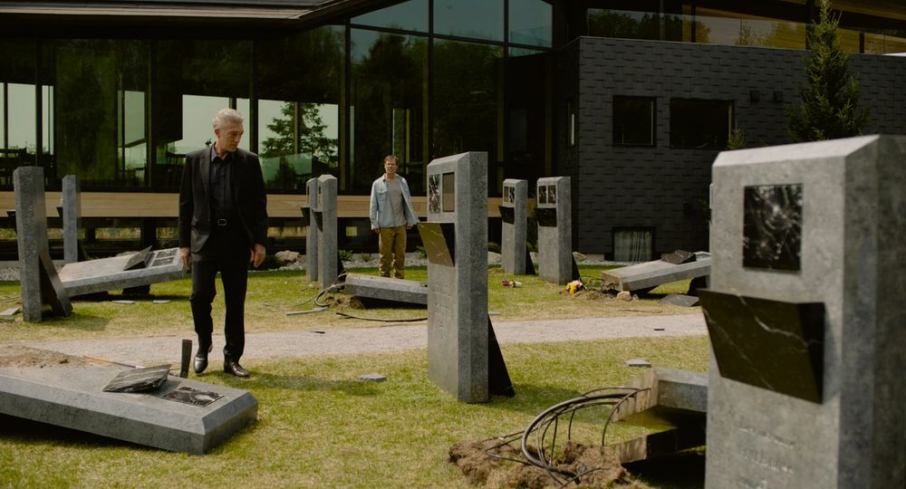 Screenshot from the film "The Shrouds" (2024) directed by David Cronenberg. In the scene, the lead character (played by Vincent Cassel) is in the middle of a cemetery where the tombstones allow visitors to view live footage of the deceased underground. Someone has vandalized the the cemetery and destroyed some of the tombstones - in the image, the lead character is observing the damage.