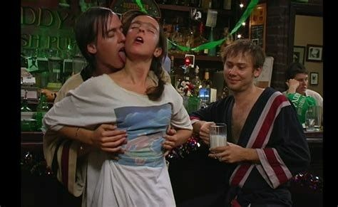 This is a screenshot from It's Always Sunny In Philadelphia. There is a very gross and incestuous family on the show called the McPoyles. This image is of three of the McPoyles in Paddy's Pub, the bar the show takes place in. They're dressed in robes and nightshirts. One of the McPoyle men is embracing his sister from behind and licking her neck while their brother, who is drinking a glass of milk, looks on approvingly.
