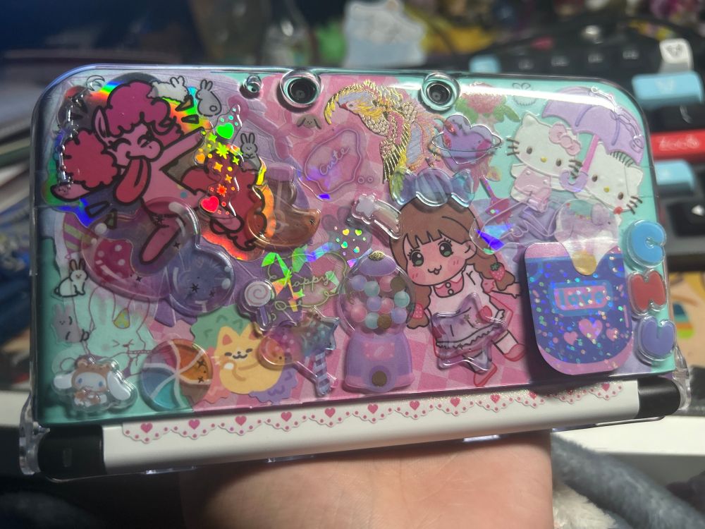 a cyan 3DS with a very decorated top cover using stickers