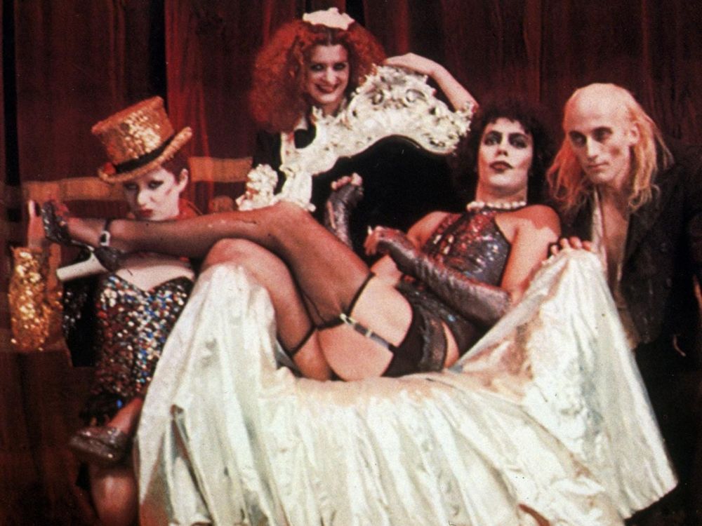 Photography still from the movie The Rocky Horror Picture Show with Dr. Frank-N-Furter sitting sideways on his throne surrounded by Magenta, Riff Raff, and Columbia