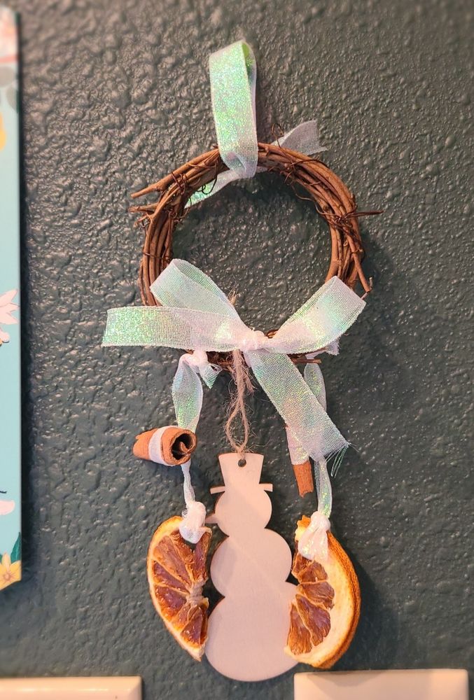 Photo of one of my small wreaths made from a 3 inch grapevine wreath, with dried orange slices, and cinnamon sticks, tied with white iridescent ribbon, and a wooden snowman ornament. 