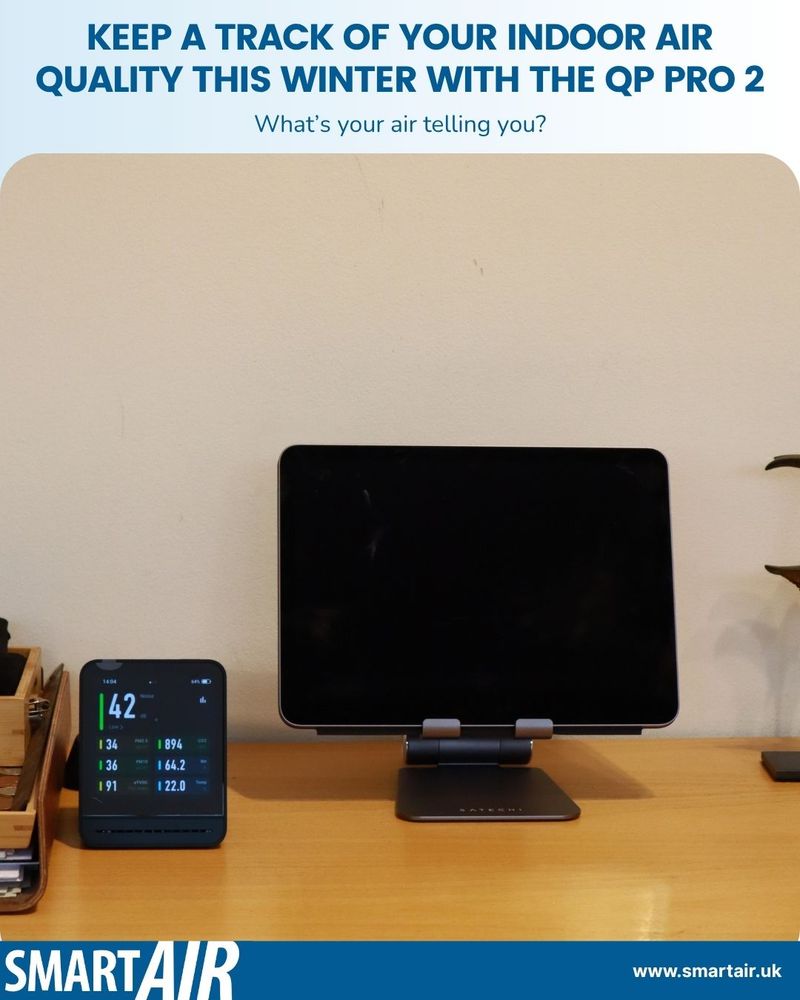 An image of a desk setup with the QP Pro 2 air quality monitor and a tablet on a stand. The monitor displays readings such as PM2.5 at 142, temperature at 19.1°C, and humidity at 64.2%. The text at the top reads: “KEEP A TRACK OF YOUR INDOOR AIR QUALITY THIS WINTER WITH THE QP PRO 2. What’s your air telling you?” The SmartAir logo and website URL (www.smartair.uk) appear at the bottom.