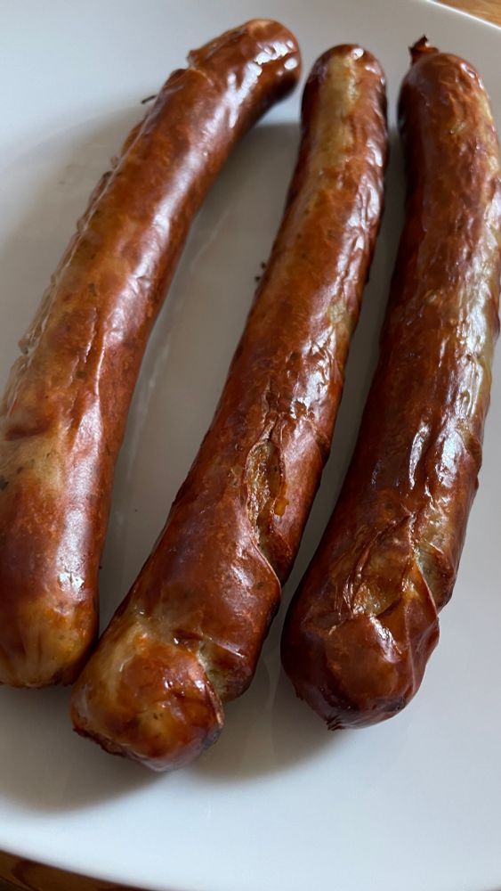 3 braun gegrillte Bratwürste auf einem weißen Teller