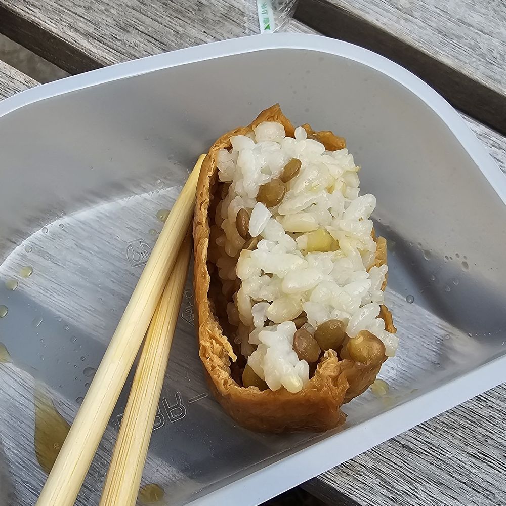 렌틸콩밥으로 만든 유부초밥 한개가 플라스틱 용기에 담겨있고 일회용 젓가락이 함께 놓여있다