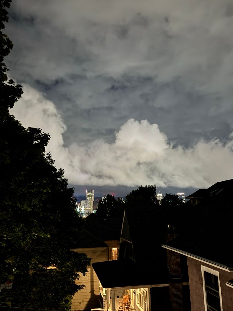 A night view from our window across the city, where big clouds are illuminated over the skyscrapers