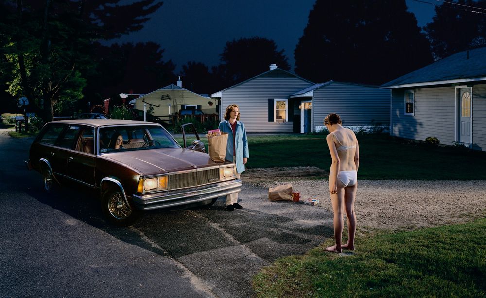 photography of a girl in her underwear standing in front of a car at night with two other women inside by Gregory Crewdson