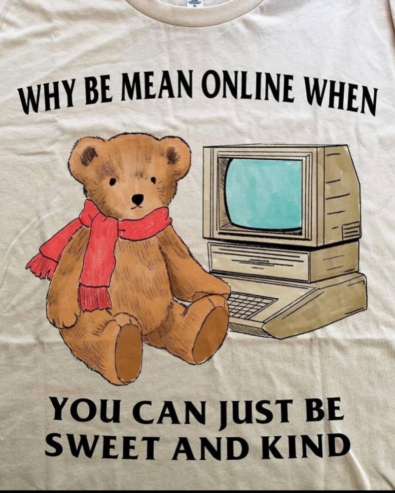 A t-shirt with a scarf wearing cartoon bear sat in front of an old desktop computer that says “why be mean online when you can just be sweet and kind”