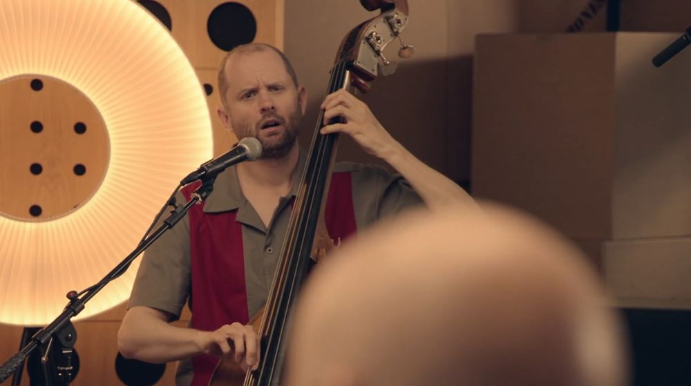 A still of Willip squinting at Alex while playing the cello