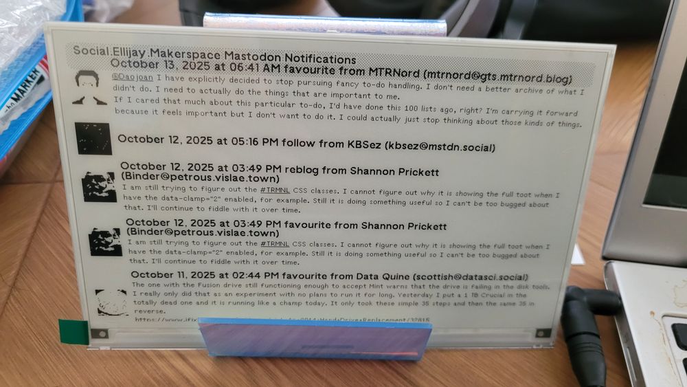 A DIY TRMNL e-ink screen sitting in a holder. It is displaying a formatted version of notifications from the same Mastodon account posting this.