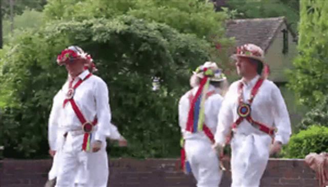 a group of men are walking in a line wearing white shirts and hats