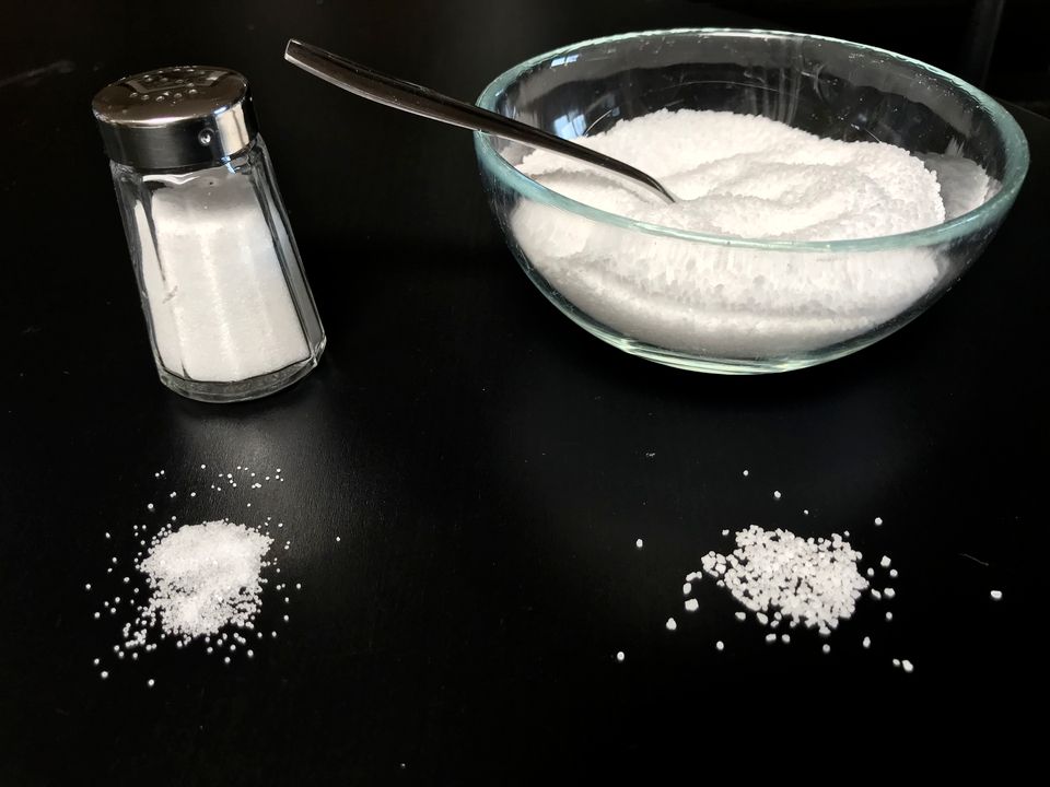 A bowl and a shaker of salt with some spilt on a black surface