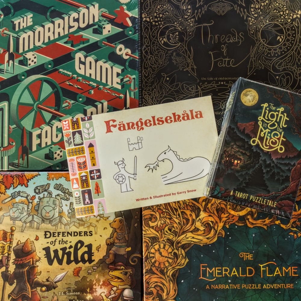 FÄNGELSEHÅLA zine on top of following board games: The Morrison Factory, Threads of Fate, The Light in the Mist, The Emerald Flame, and Defenders of the Wild.