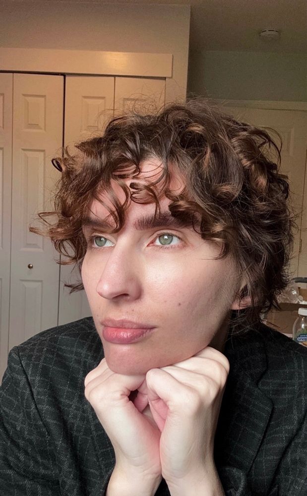 Selfie of the poster. They have short curly brown hair and wear a plaid blazer.