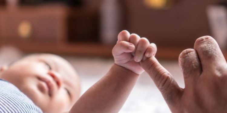 A baby holds tightly onto an adult's little finger. 