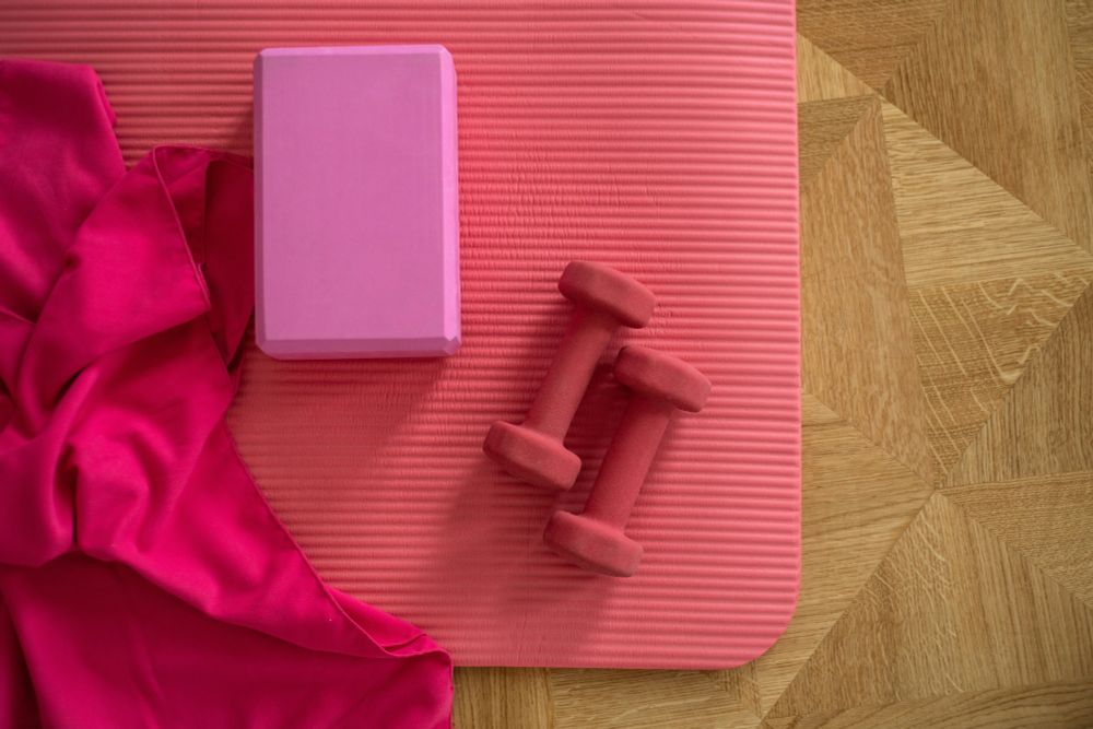 Two weights, an exercise block and towel lie on a pink exercise mat.