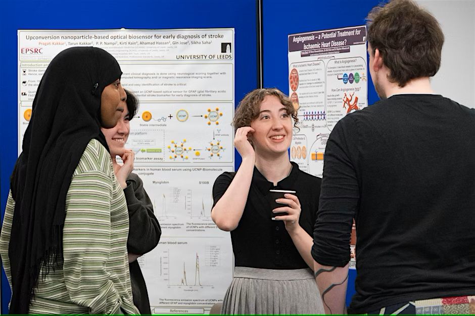 Four people standing and conversing in front of two scientific posters at an academic event. 