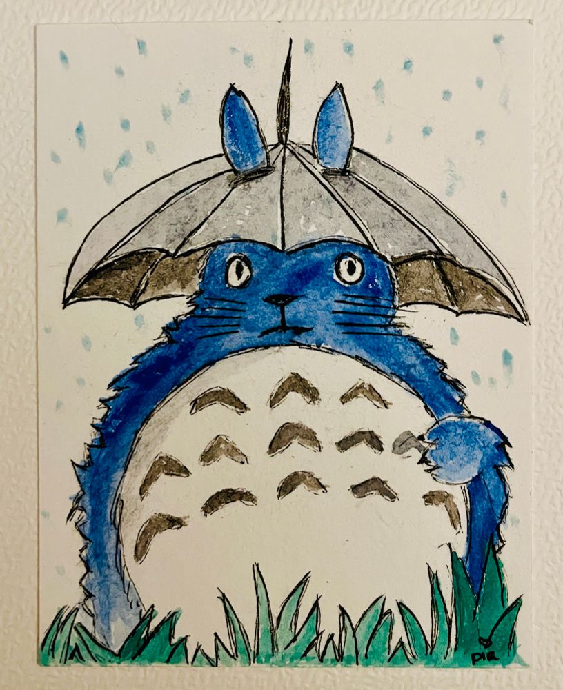 ATC Hochformat. Aquarellzeichnung Totoro im Regen mit Regenschirm steht im grünen Gras. Totoro ist blau mit weißem Bauch. Auf dem oberen Bauch sind schwarze Bumerang ähnliche Flecken.  Der Schirm ist grau. Oben aus dem Schirm gucken die blauen Ohren von Totoro raus. 
