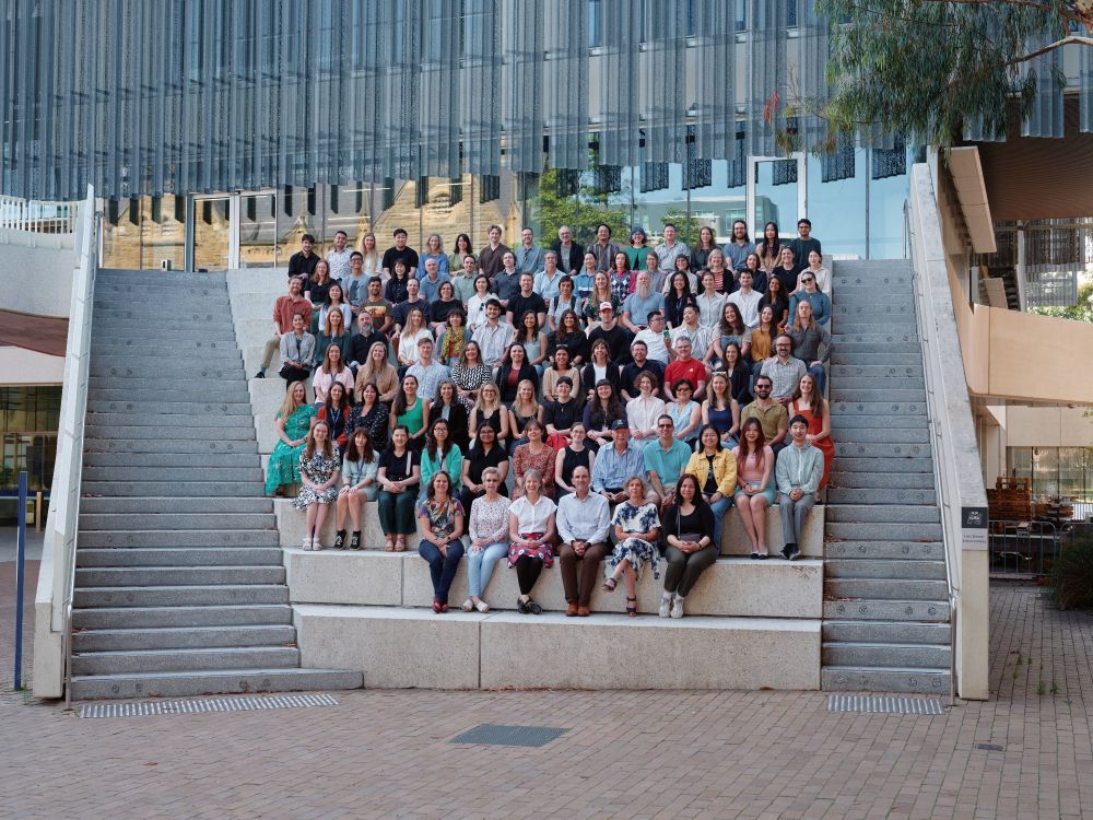 A large group of staff from MSPS sit on concrete steps outside a modern building.