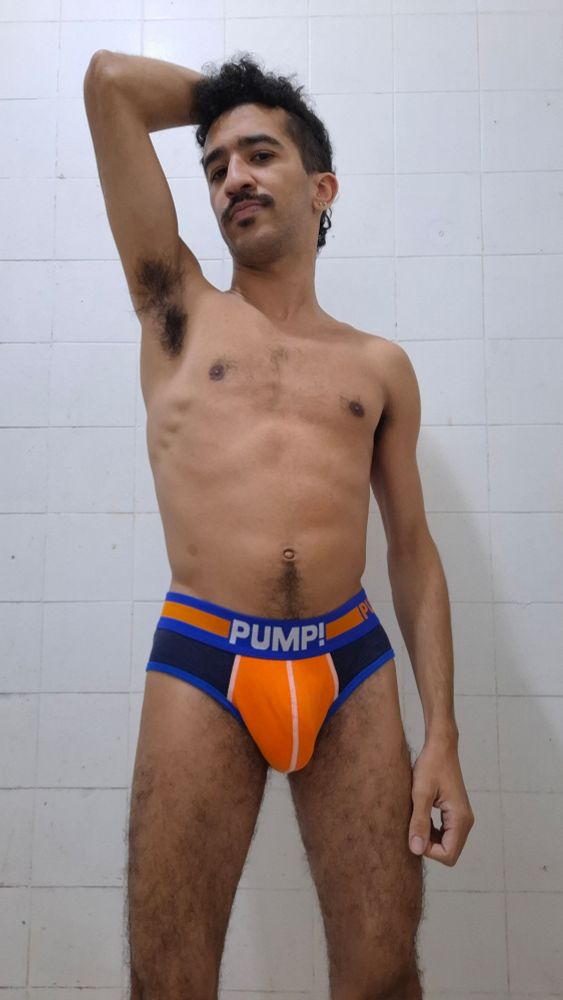 Foto minha usando uma cueca pump laranja e azul e mostrando o suvaco