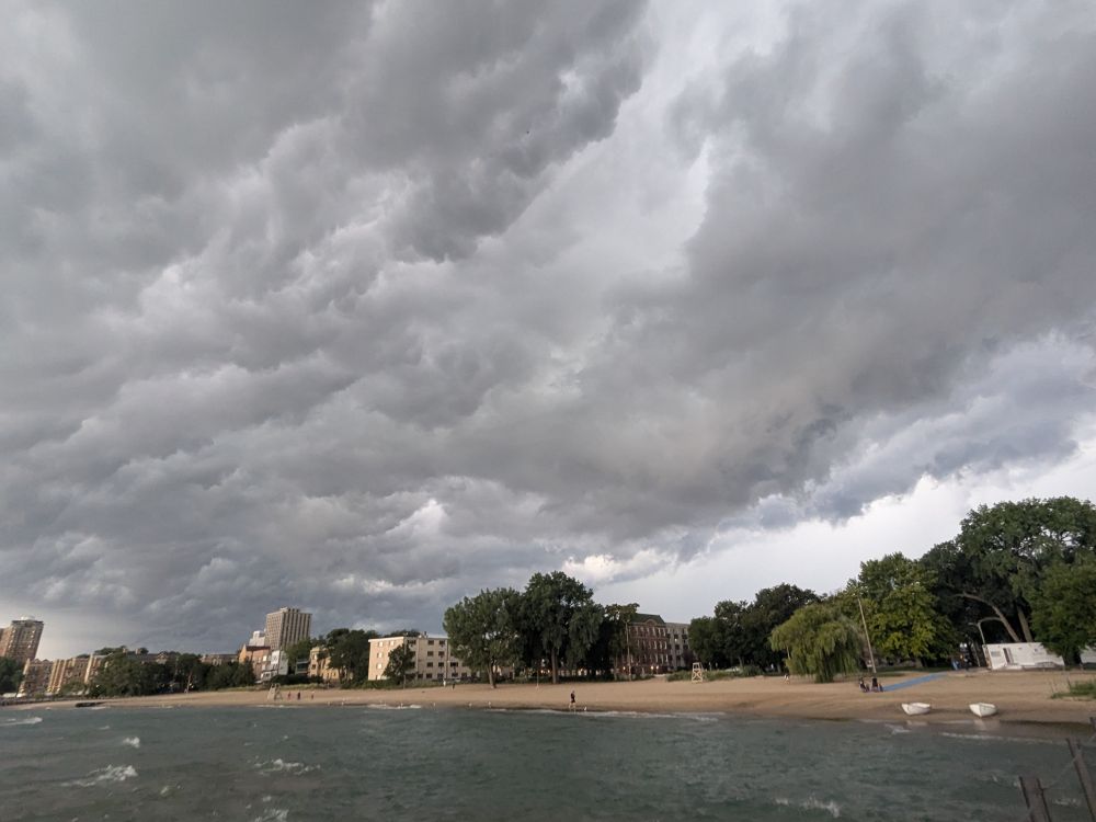 A photo of dramatic gray storm clouds over a beach with city buildings behind it