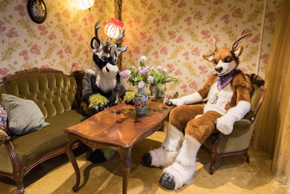 A caribou and a deer sitting at a table in a 1920's style living room.