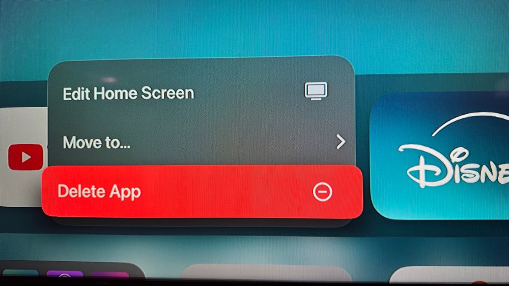 A photograph of a television showing the Apple TV interface where the Disney app is being deleted