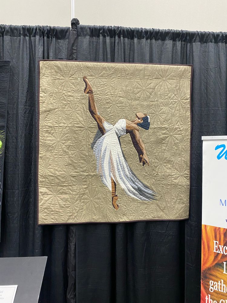 A quilt featuring a Black ballet dancer in a pose: her arms are back, her back is arched and her leg is in the air as the other is en pointe. 

Ballerina Girl by Debra Lathan
Quilted by China Oiler
Missouri City, TX
USA
Techniques: Hand embellishment; machine piecing and quilting; paper piecing
Design Source: Prima Ballerina pattern by
Veruschka Zarate
Ballerina Girl was inspired by my niece, Lauren Campbell (age 18), who has danced since the age of two. Her love of dance exudes grace and poise. She has inspired young African American girls to learn and enjoy the art of ballet.