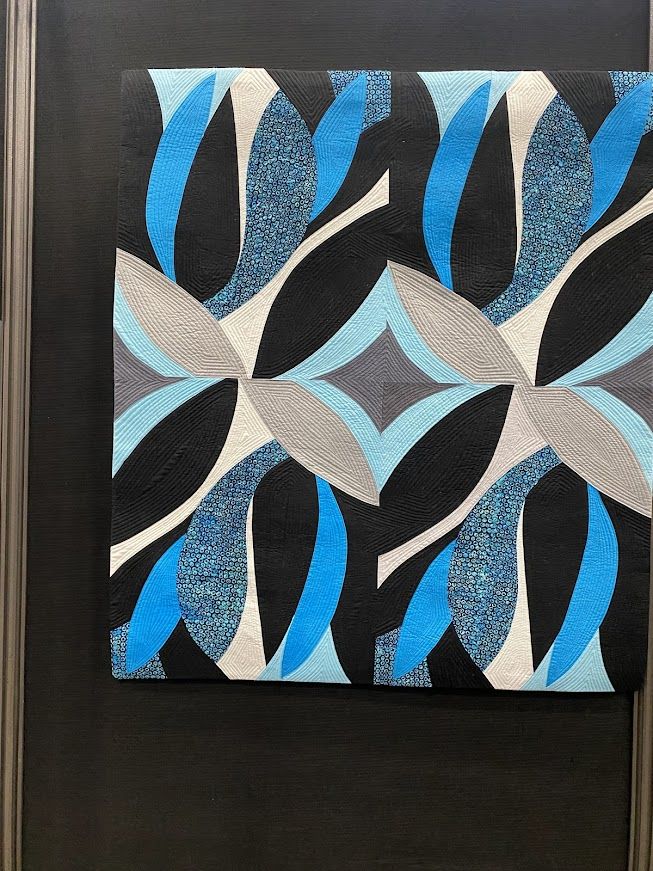 A quilt in organic waves of black and blue and cream and gray evoking a little bit of the Matisse cutouts. 

SAQA: NOW-Contemporary Art Quilts of Today
Kaleidoscope Joy
Carole Rossi
Sacramento, CA
USA
AVAILABLE FOR PURCHASE
Techniques: Pattern created by the artist based on original sketch; machine pieced and quilted
Materials: Commercial batiks and solid cotton fabrics; various rayon threads
Restricting myself to a limited color palette, I have made what I hope viewers experience as a lively and creative composition, evoking spontaneous joy and movement. I drew the original design in my sketchbook while in London on a bright and windy day. A rare blue sky with white clouds dominated the scene, along with gray buildings, black rooftops, and the ubiquitous black London taxis.