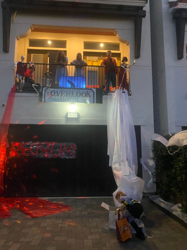 An Shining themed Halloween decor above a garage door.  A ramp from the balcony delivers candy to two trick or treaters. 