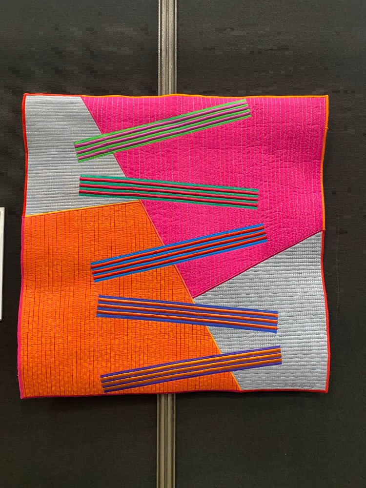 A quilt of large pink and orange and grey background blocks with five groups of striped blocks on top of them. 

SAQA: NOW - Contemporary
Art Quilts of Today
Dimensions #9
Michele Hardy
Silverthorne, CO
USA
AVAILABLE FOR PURCHASE
Techniques: Surface design (dye, paint, screenprinting); machine stitching
Materials: Hand-dyed and painted cotton fabrics; cotton batting; dye; paint; assorted threads
I love color...and lines...and shapes...and fabric... and dye...and thread. Portraying simple shapes at different scales, overlaying and overlapping, and using vibrant color and contrast, I create a new world of abstract forms that combine to make a whole.