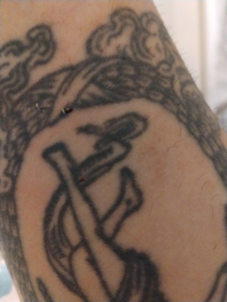 Bottom half of forearm tattoo of tarot card 'The World" with two puncture wounds