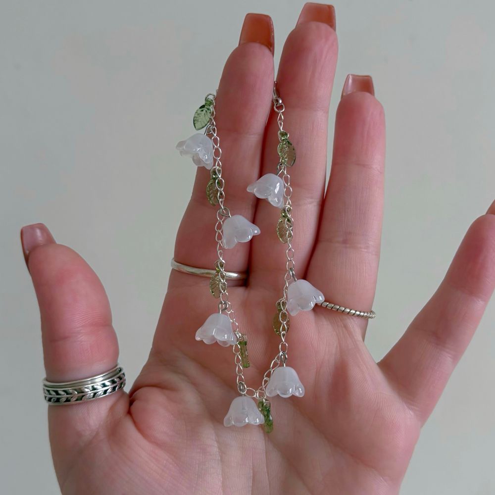 hand holding up a bracelet with white flower caps and green leaves on silver chain