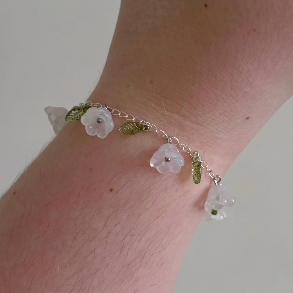 close up of a bracelet with white flower caps and green leaves on silver chain while being worn