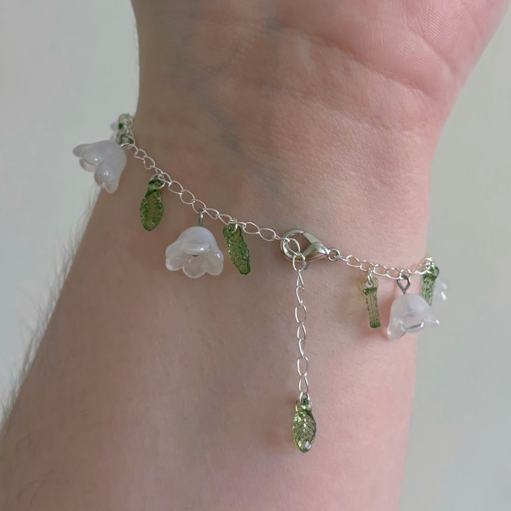 close up of the closing of a bracelet with white flower caps and green leaves on silver chain while being worn