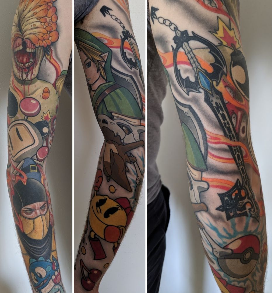 A composite image showing three views of a colorful full sleeve tattoo featuring a variety of distinct illustrated figures and objects. The left section includes a grotesque figure with exposed mouth and fungal growth, a character with a large, light-colored square cartoon face with two vertical lines for eyes, a close-up of a figure wearing a black hood and a yellow mask over the lower part of their face, framed by orange flames, and features a vibrant blue, happy, dragon-like cartoon creature with large eyes, sitting atop a bubble. The middle section shows a central green-clad character with blonde hair, below which is a brown, dinosaur-like creature with a skull on its head and a bone in hand, and a large round yellow character. The right side prominently displays a large, ornate stylized key weapon surrounded by flames and electrical-like energy, with a round red and white ball near the bottom.