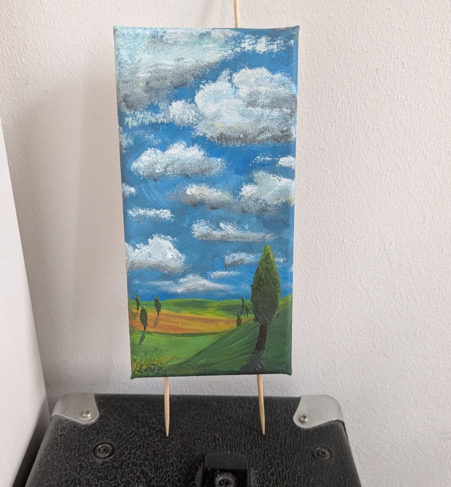 Ein Foto eines kleinen Ölgemäldes in Hochformat ist an Holzstäben befestigt und an eine Wand gelehnt. Es zeigt eine leicht hügelige Landschaft mit vereinzelt spitzgewachsenen Bäumen die einen langen Schatten in Richtung des Betrachters werfen. Der Himmel ist gespickt mit fluffigen Wolken das ca zwei Drittel des Bildes einnimmt. Die Farben sind weiss, blau, sandgelb, grün braun 