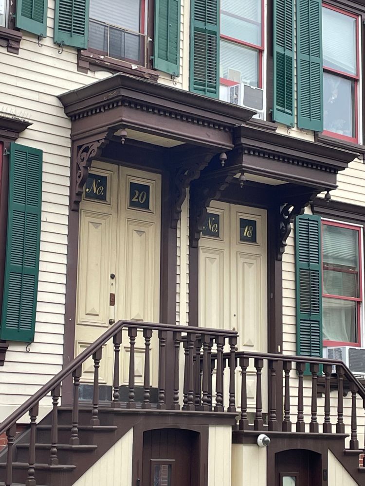 Two adjoining footsteps of the houses with wooden carvings around the doors and windows with the house numbers painted on them 