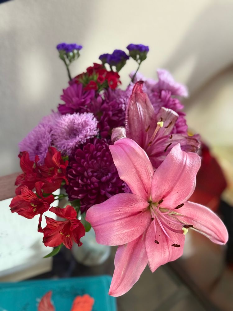 A vibrant bouquet featuring 2 large pink Lilies, red Alstroemeria, pink and purple Chrysanthemums, and purple Statice flowers.