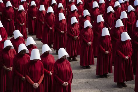 A picture of several women wearing red dresses with white hats, reflecting the handmaid‘s tale a book by Margaret Atwood