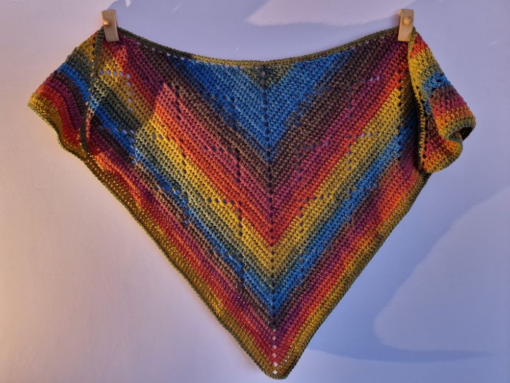A crochet shawl in muted rainbow colours.